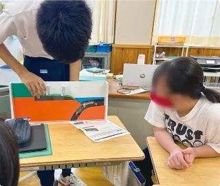 机の上に立てた色分けの模型を見ている生徒たち
