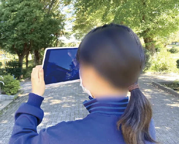 屋外でタブレットを使って観察している生徒