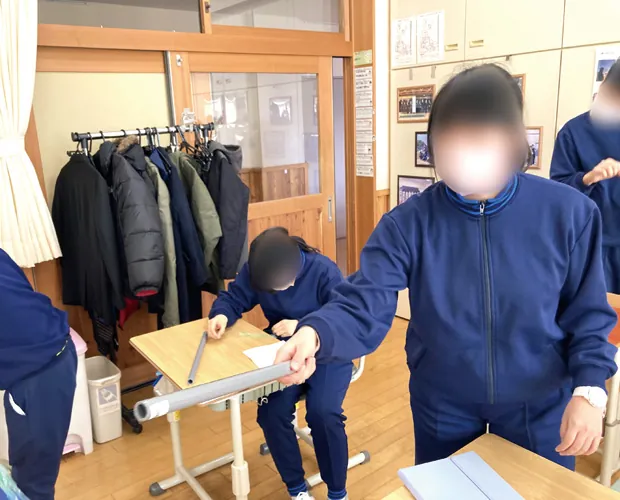 筒状の器具を机の上で使って観察している生徒たち