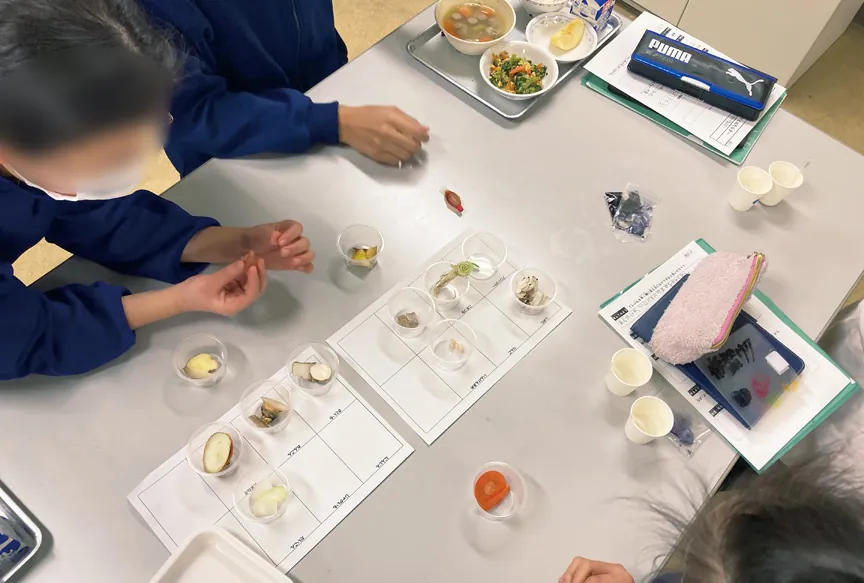 給食の食材を小さな容器に分けて並べ、でんぷんについて調べている生徒たち