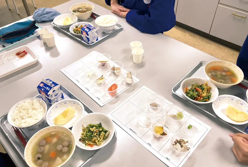 給食（ごはん、汁物、おかず、牛乳）と、食材を小さな容器に分けて並べたワークシート