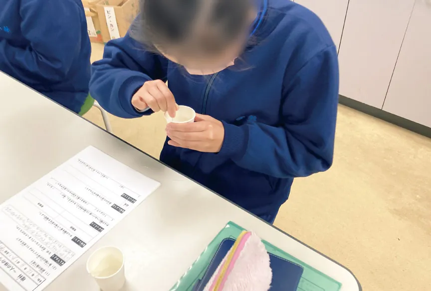 小さなカップの中身をスプーンで混ぜている生徒