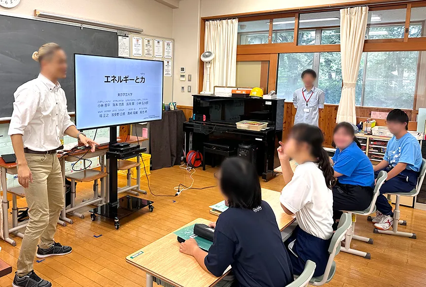 「エネルギーと力」のスライドの前で説明する先生と、話を聞く生徒たち