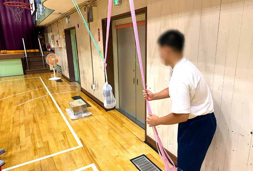 体育館のギャラリーから吊るした巨大振り子のひもを持つ生徒