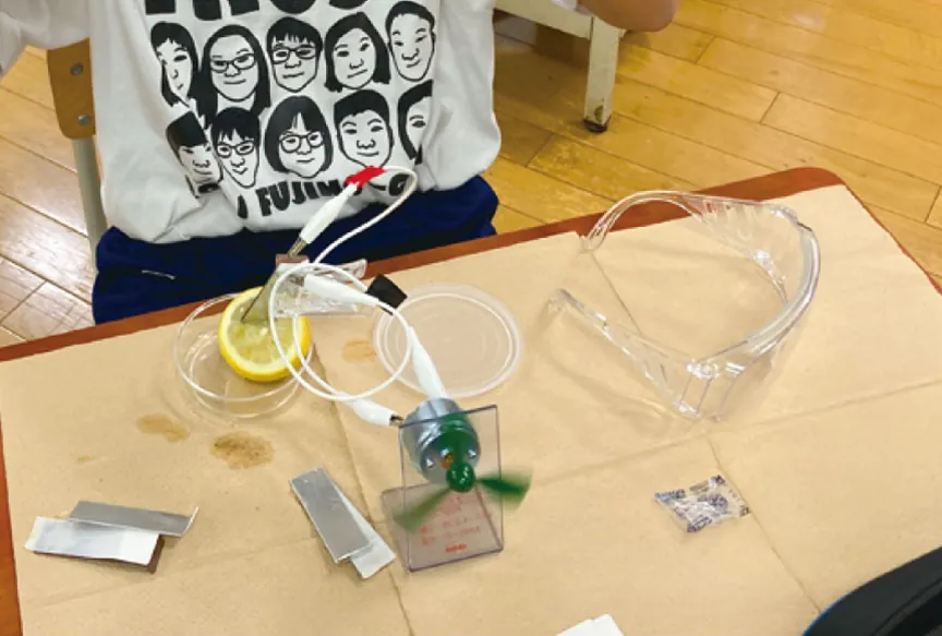 レモンと金属板、リード線、プロペラ付きのモーターで作ったくだもの電池と、保護めがね