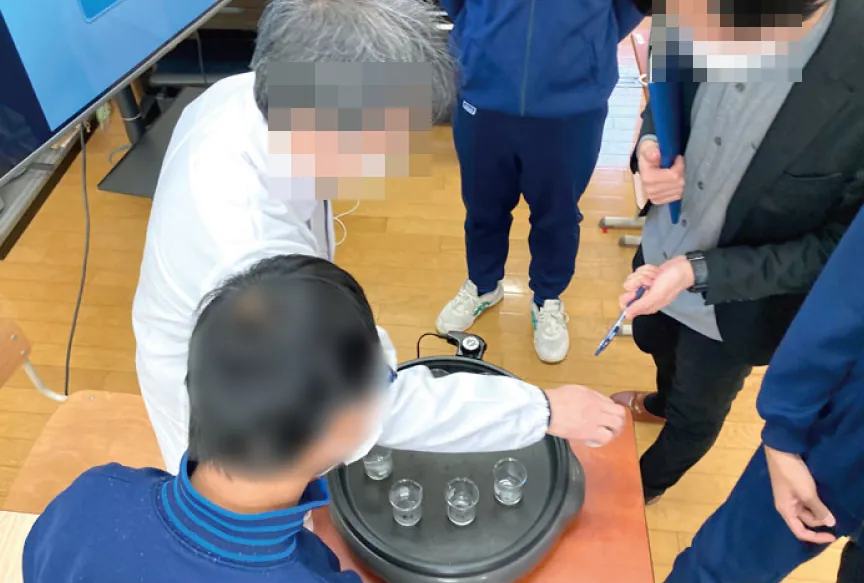 ホットプレートに並べたビーカーの水を蒸発させる様子を、先生と生徒が見ている
